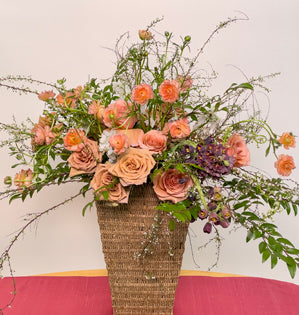 An overflowing basket design created with spirea, huckleberry, butterfly ranunculus, Moab and Toffee garden roses, fritillaria, and delphinium belladonna.