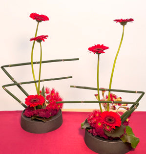 Dynamic matching modern designs in shades of red created with, gerbera daisies, gum tree eucalyptus, snake grass, hanging amaranthus, and galax leaves.