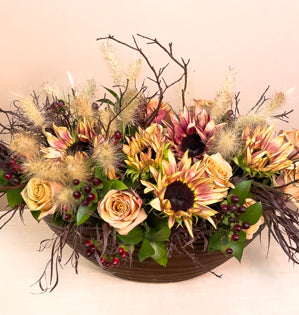 A large rustic compote full of manzanita branches, ruscus, agonis, hypericum berries, bunny tail grass, golden mustard roses, and sunflowers.