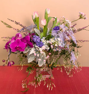 A fabulous compote design abundant with jasmine vine, hydrangea, dyed plumosa, fringed tulips, allium, heather, dusty miller, hyacinth, and phalaenopsis orchids.