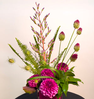 A striking linear design made by combining hot pink dahlias, bromeliad, sword fern, nigella, camellia, galax leaves, allium, and lily grass.