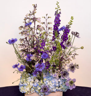 An abundant vegetative design in shade of purple and blue made with, hydrangea, foxglove, larkspur, bachelor buttons, and nigella.