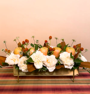 A beautiful long centerpiece full of apples, Eugenie garden roses, gomphrena, eyelash clematis, Italian ruscus, magnolia leaves, and galax leaves.